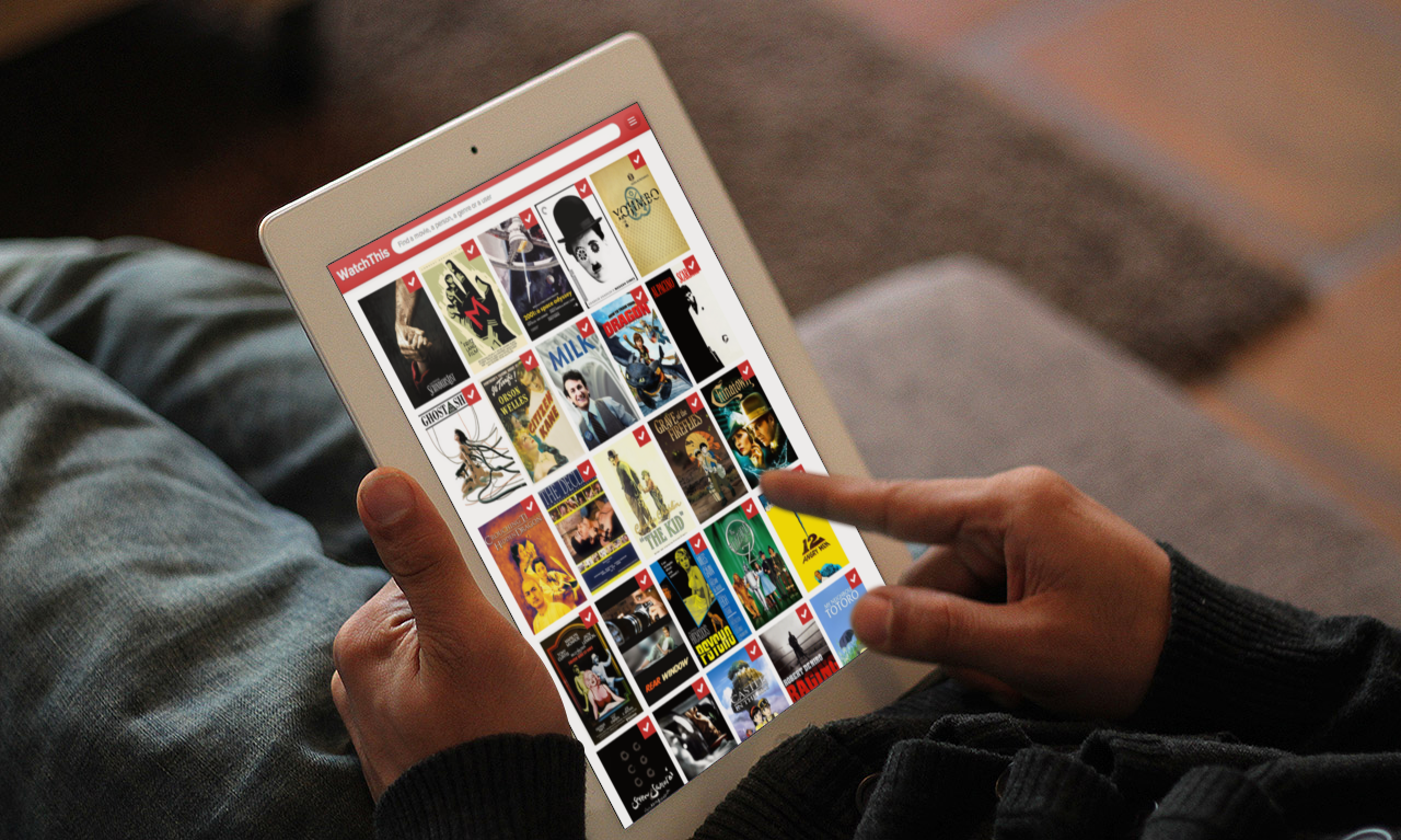 Person laying on a couch, interacting with an iPad that lists 20 movie posters including Shindler's List, Ghost in the Shell and The Kid.