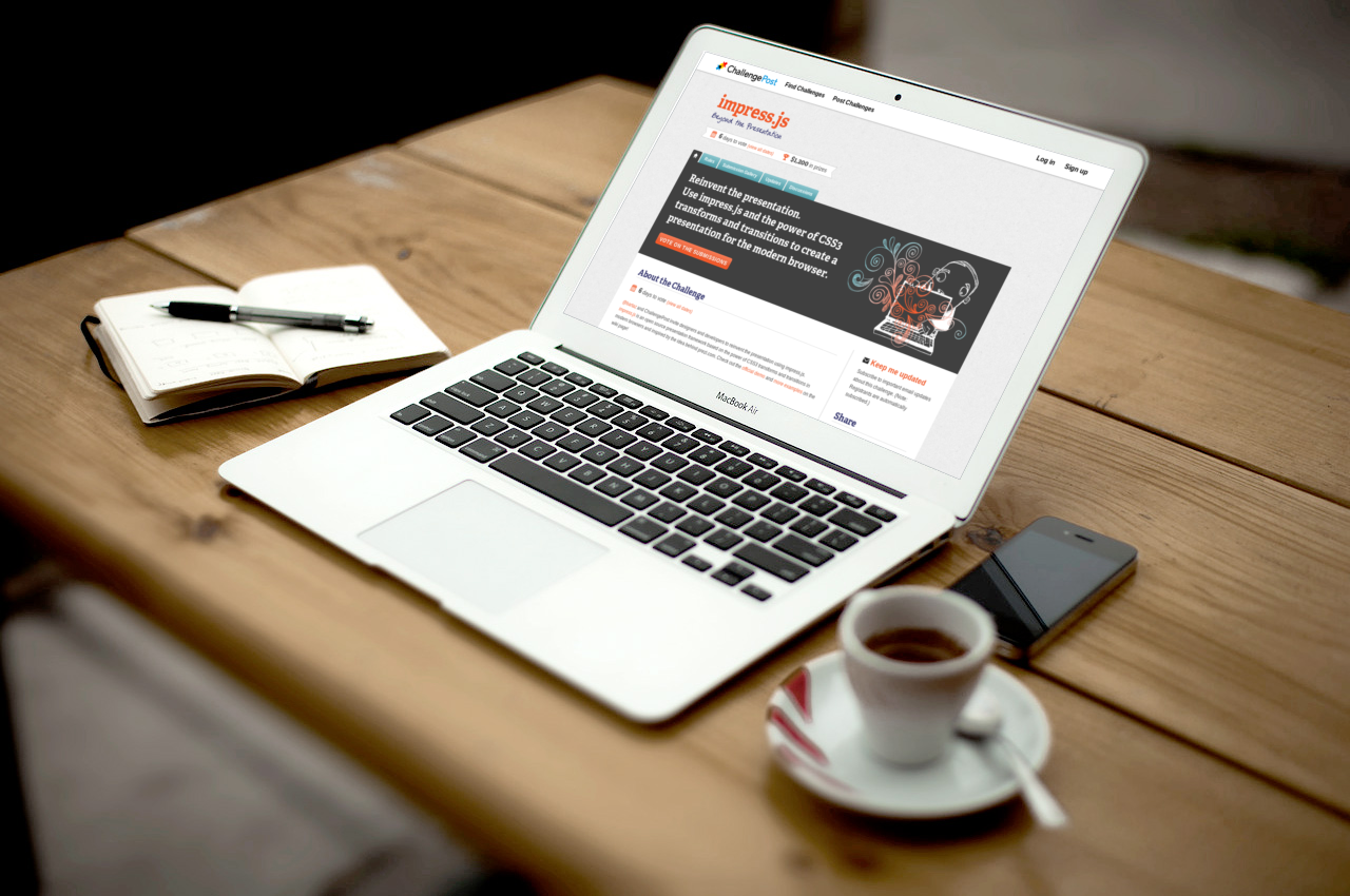 A MacBook Air on a wooden table next to an open notebook, an iPhone and an espresso. The MacBook has a hackathon homepage open, inviting developers to 'reinvent the presentation using impress.js and the power of CSS3'.